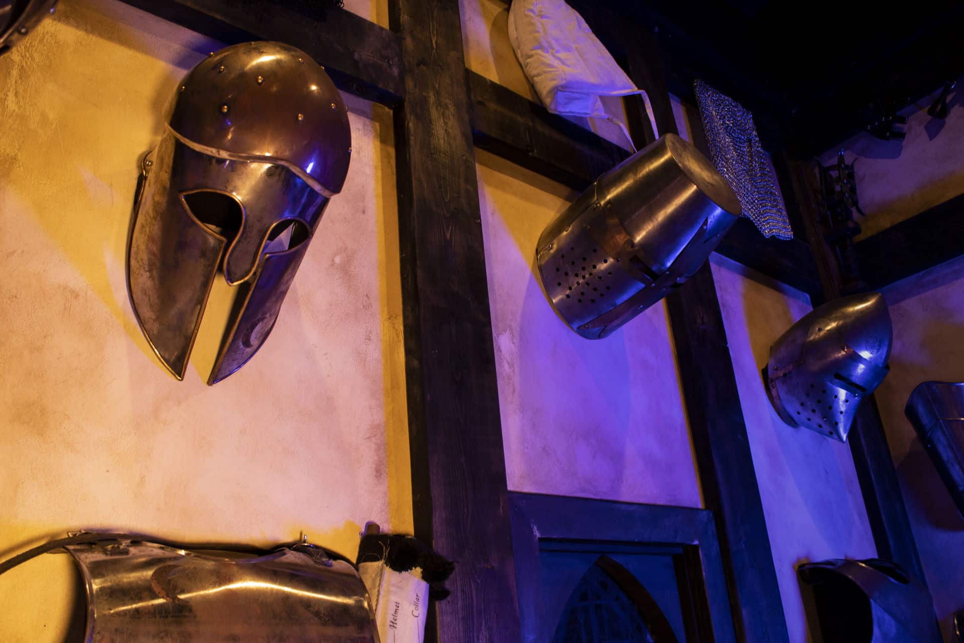 Metalhead A close up of three iron helmets hang at the top of the wall of the armory.