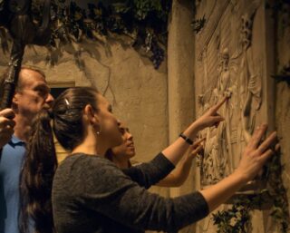 The players examine a stone fresco depicting a few of the various gods.