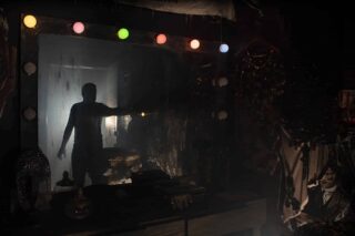 A photograph showing the dressing room in the dark with only the vanity lights illuminating a shadowy figure in the doorway.