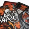 Three cards from Cards At War are fanned out on a table with a card box in the foreground.
