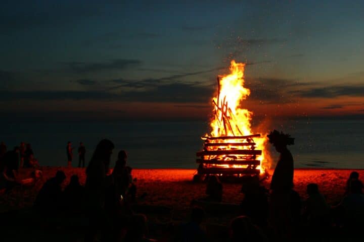 A photograph of a bonfire, illuminating silhouettes of surrounding people.