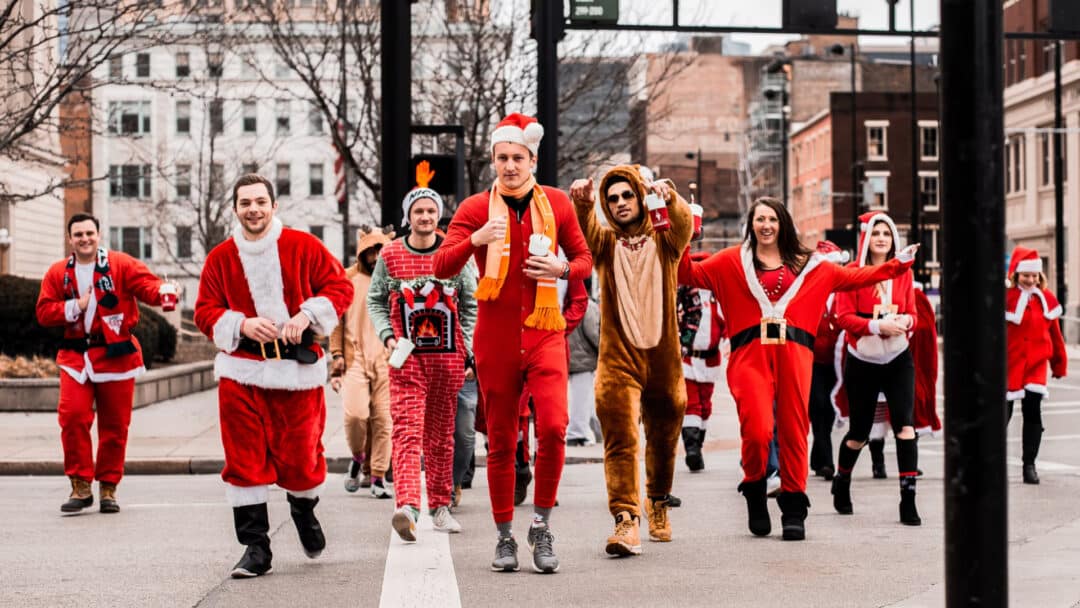 A group of people in Christmas costumes walking down a street.