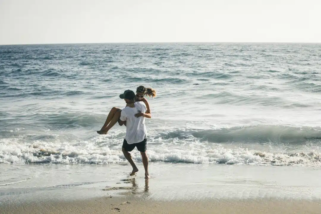 A man carries a woman across the beach.
