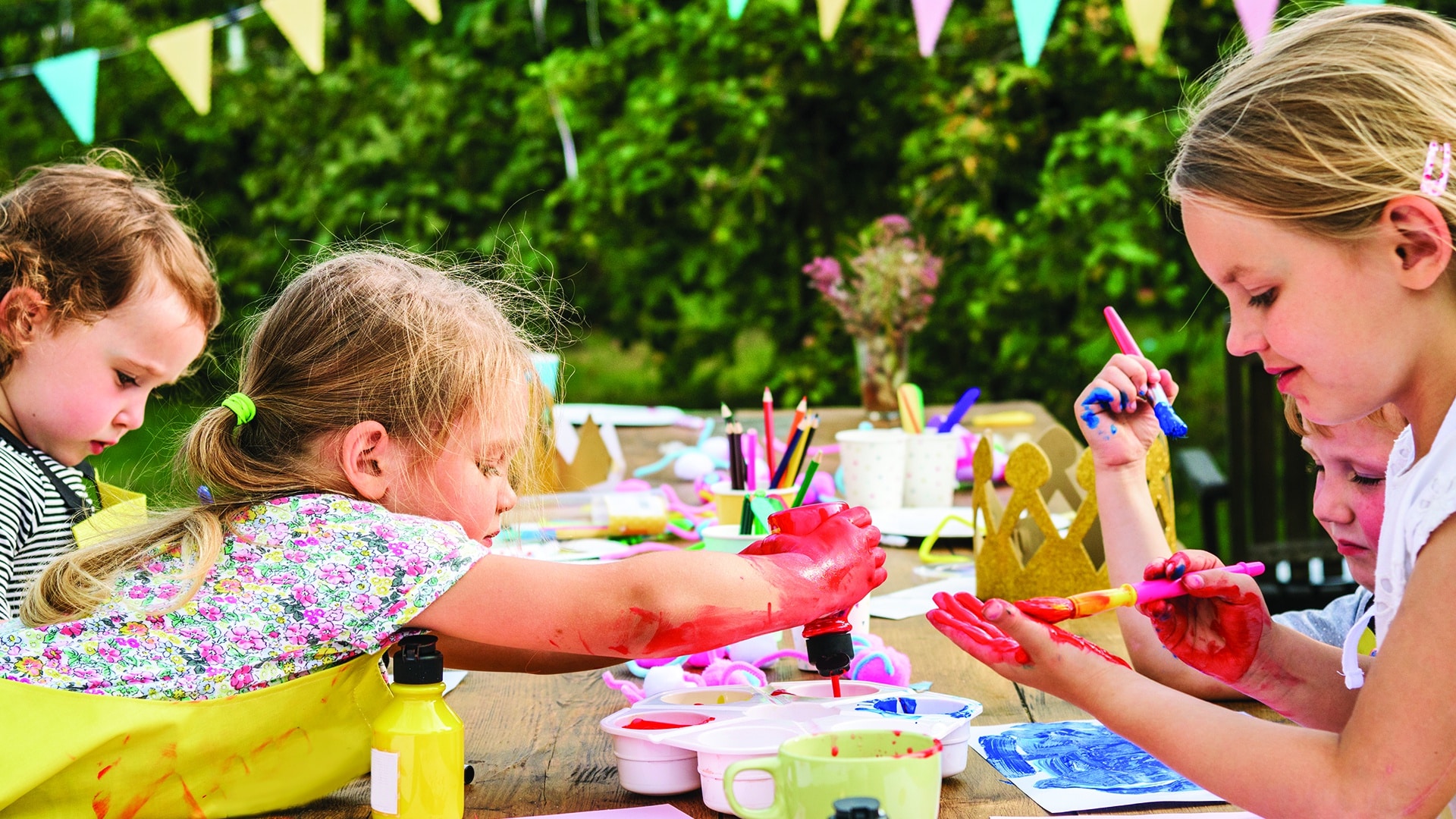 A group of children painting on a picnic table outdoors.