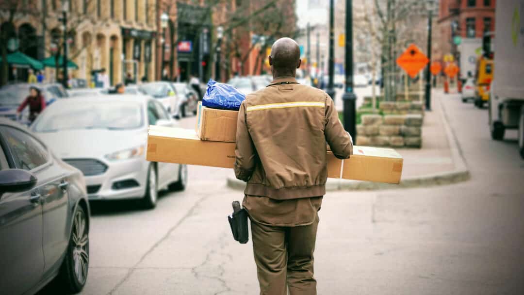 A man delivering packages walks down a sidewalk.
