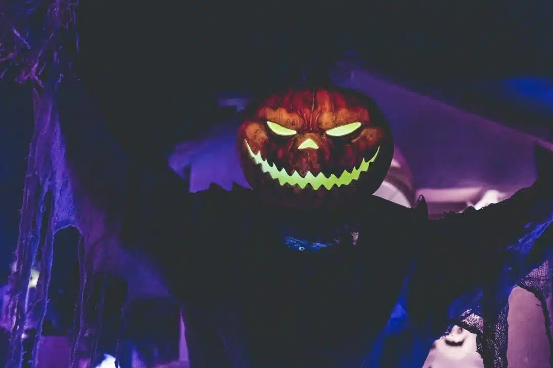 A shadowy figure with a pumpkin head stands menacingly against a purple lit background.