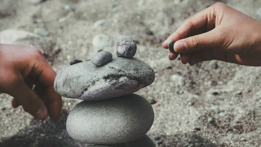 Two hands stack rocks on a beach.