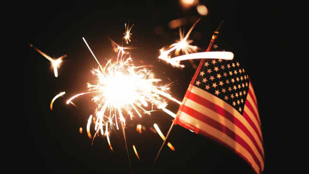Celebrating the 4th of July with a sparkler and American flag in hand.