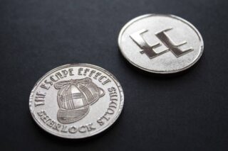 Two coins depicting a deerstalker hat and The Escape Effect logo