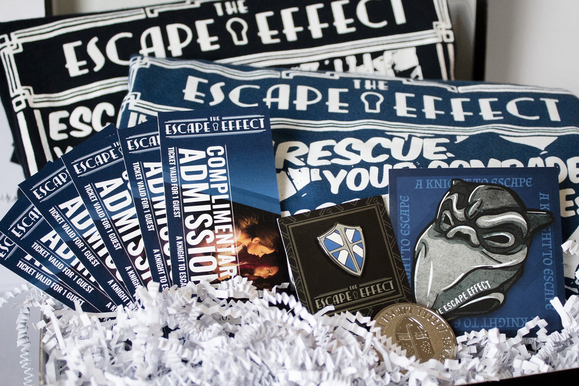A gift box including tickets, sticker, pin, coin and shirts.