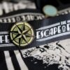 A "The Escape Effect" lanyard with a compass lapel pin attached.