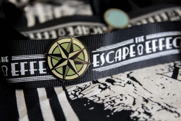 A "The Escape Effect" lanyard with a compass lapel pin attached.