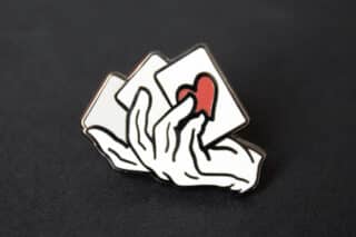 A close up of a magician's hand and cards lapel pin.