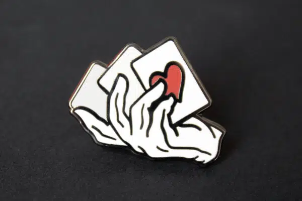 A close up of a magician's hand and cards lapel pin.