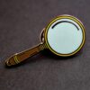 A close up of a magnifying glass lapel pin.