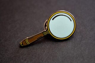 A close up of a magnifying glass lapel pin.