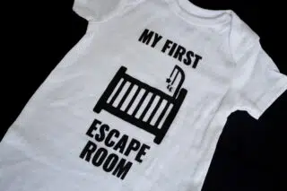 A photo showing a baby onesie with the phrase My First Escape Room.