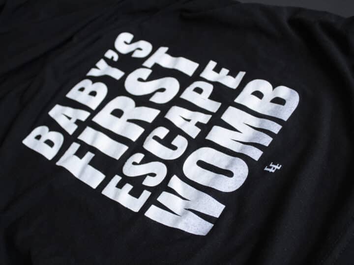 A photo showing a maternity shirt with the phrase Baby's First Escape Womb.