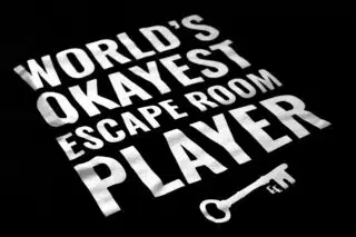 A photo showing a shirt with the phrase World's Okayest Escape Room Player.