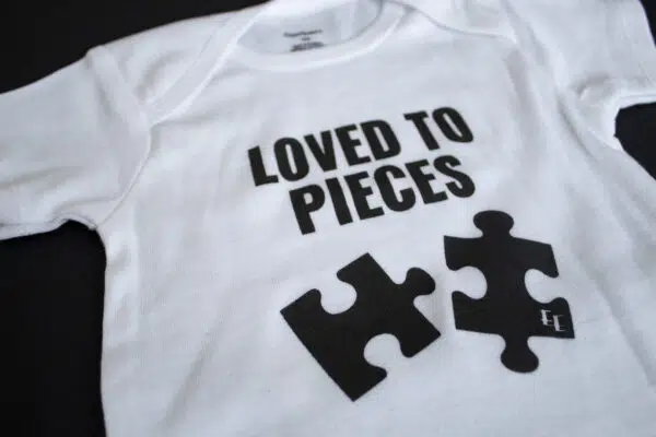 A photo showing a baby onesie with the phrase Loved To Pieces with puzzle pieces.