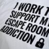A photo showing a shirt with the phrase I Work To Support My Escape Room Addiction.
