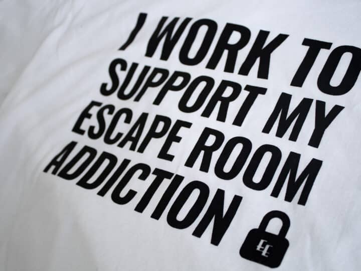 A photo showing a shirt with the phrase I Work To Support My Escape Room Addiction.