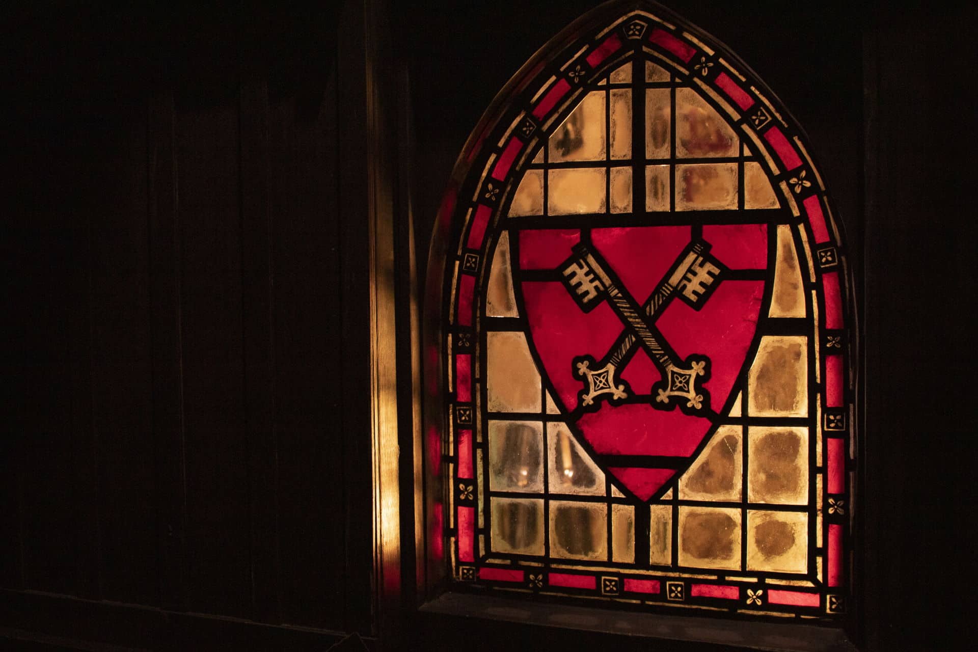A close up of a stained glass window decorated with a two keys crossing on a red shield.