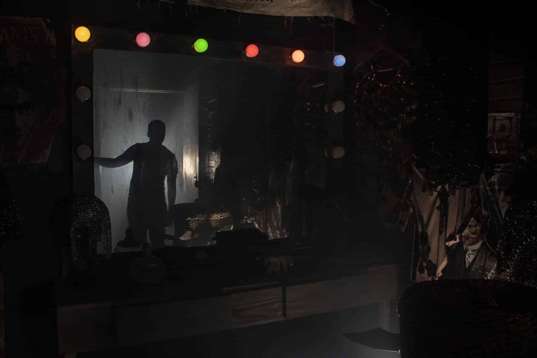 A photograph of the dressing room in the dark with only the vanity lights illuminating a shadowy figure in the doorway.