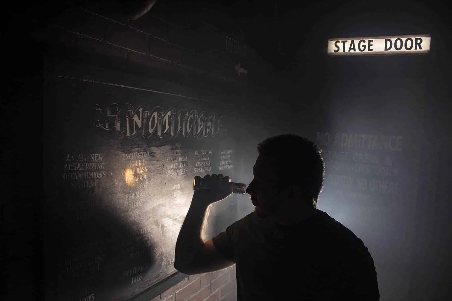 A photograph of a silhouette inspecting a noticeboard with magic show tour names on.