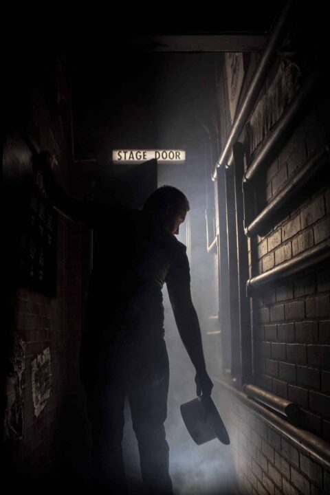 A photograph of a silhouette in front of the stage door holding a top hat.