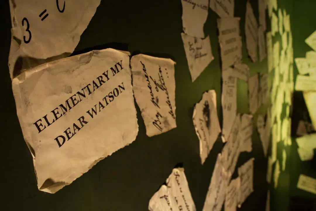 A close up view of one of many hand scribbled notes along that wall reading,"ELEMENTARY MY DEAR WATSON".