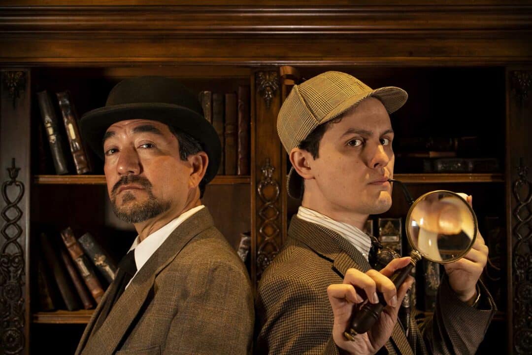 The Game Is Afoot Sherlock and Watson standing in front of a bookcase filled with old leather bound books.