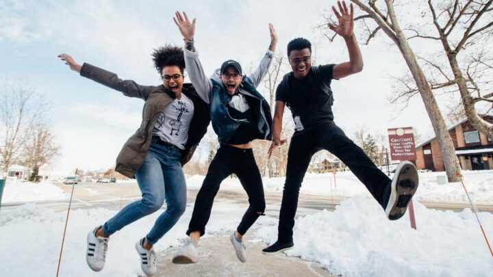 A photograph featuring three college students jumping on a snowy sidewalk.